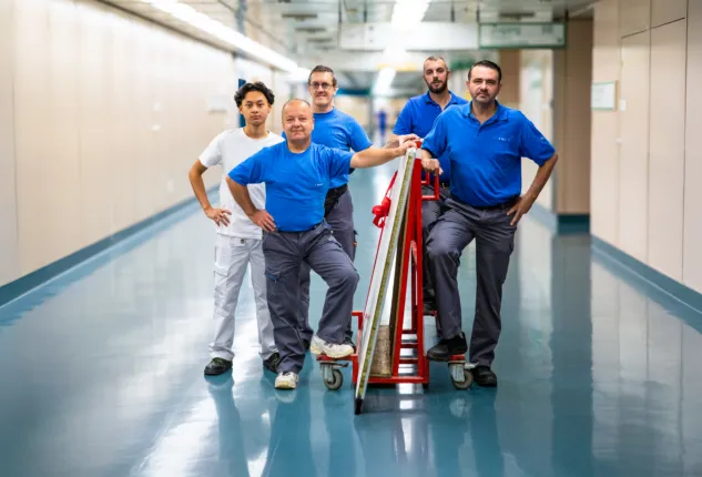 Eine Gruppe von fünf Männern stehen mit einem Rollwagen im Krankenhausflur.